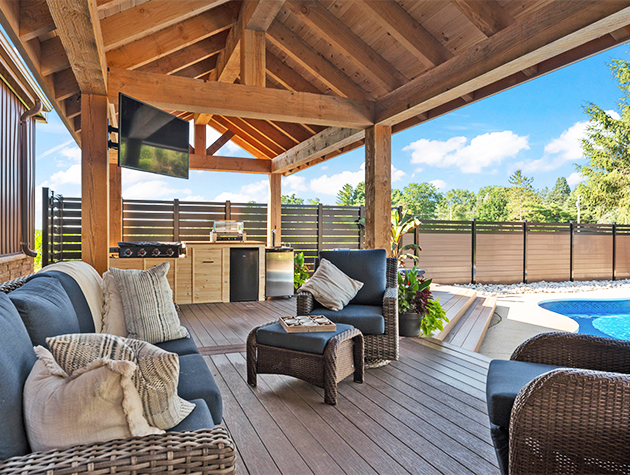 Poolside outdoor living space with outdoor furniture, tv, outdoor kitchen, and custom-built pavilion.